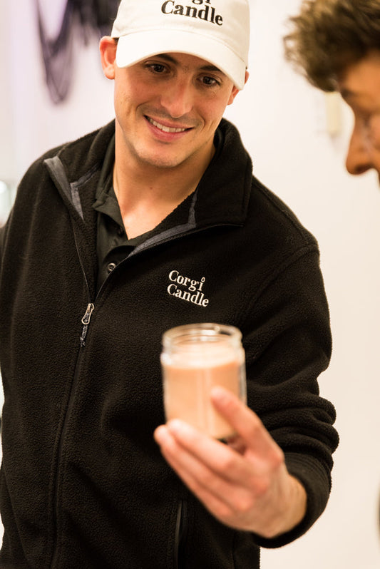 holding a strong scented soy candle while customer smells fragrance inside CORGI CANDLE in West Seneca NY
