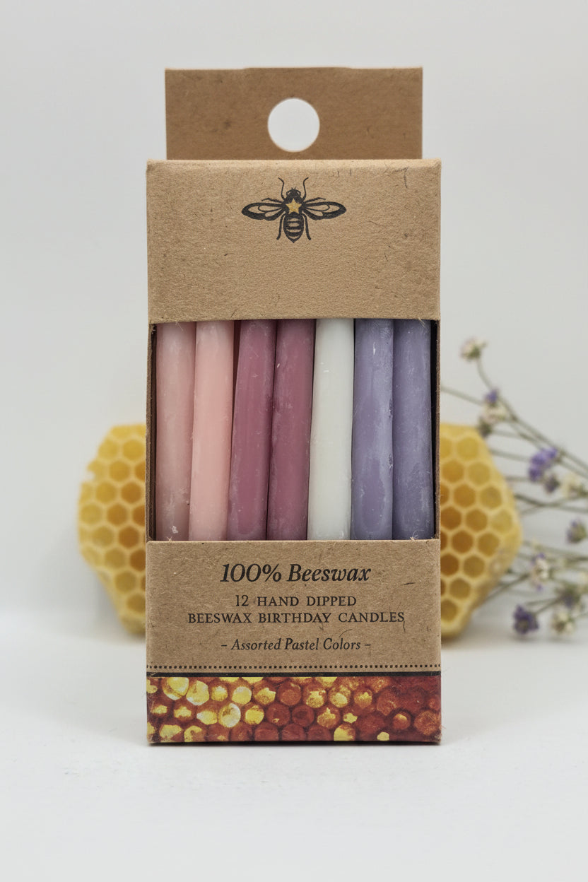 A package of 12 hand-dipped beeswax candles in assorted pastel colors, displayed in a clear windowed kraft paper box with a cardboard header.