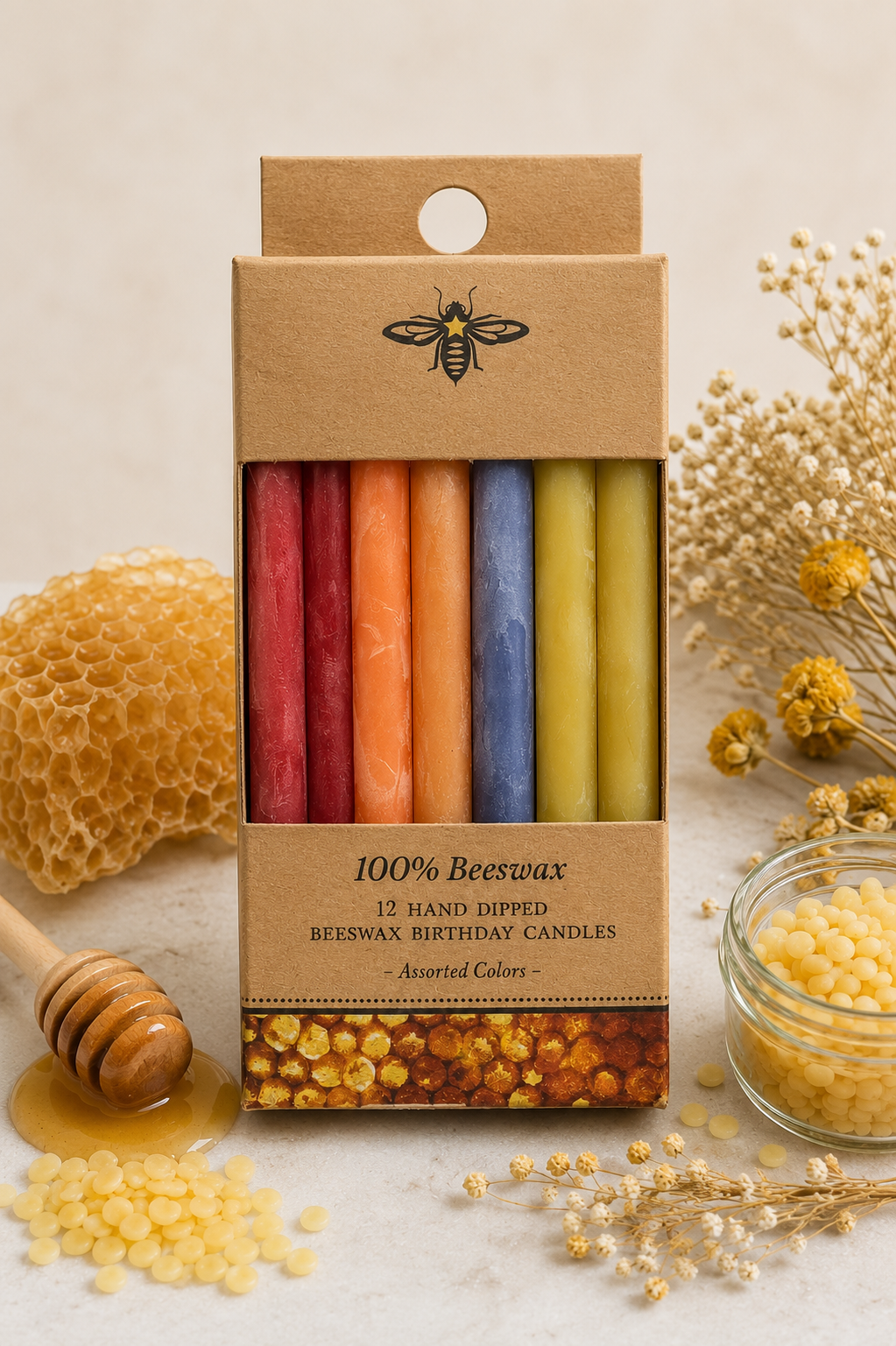 A boxed set of 12 hand-dipped beeswax birthday candles in assorted colors, displayed on a light beige surface with honeycomb, dried flowers, a honey dipper, and a small jar of beeswax around it.