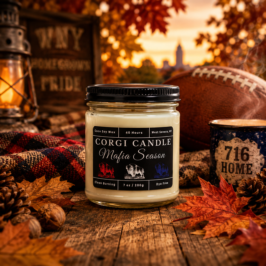 A jar candle labeled 'Corgi Candle Mafia Season' sits on a rustic wooden surface surrounded by autumn leaves, pinecones, a football, a lantern, and a mug in an outdoor fall scene.