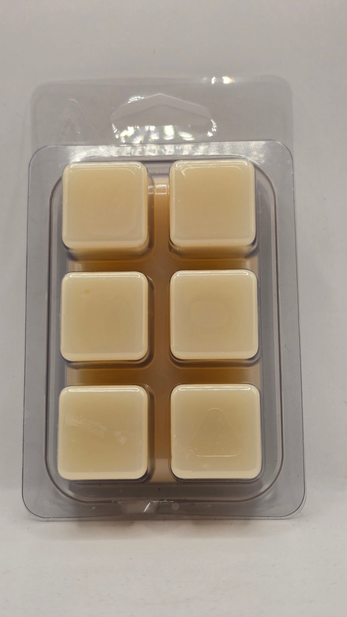 Six square cream-colored pina colada wax melts arranged in a clear plastic clamshell container. 
